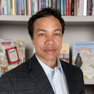 Staff Photo of a man in suit standing in front of bookshelf. 